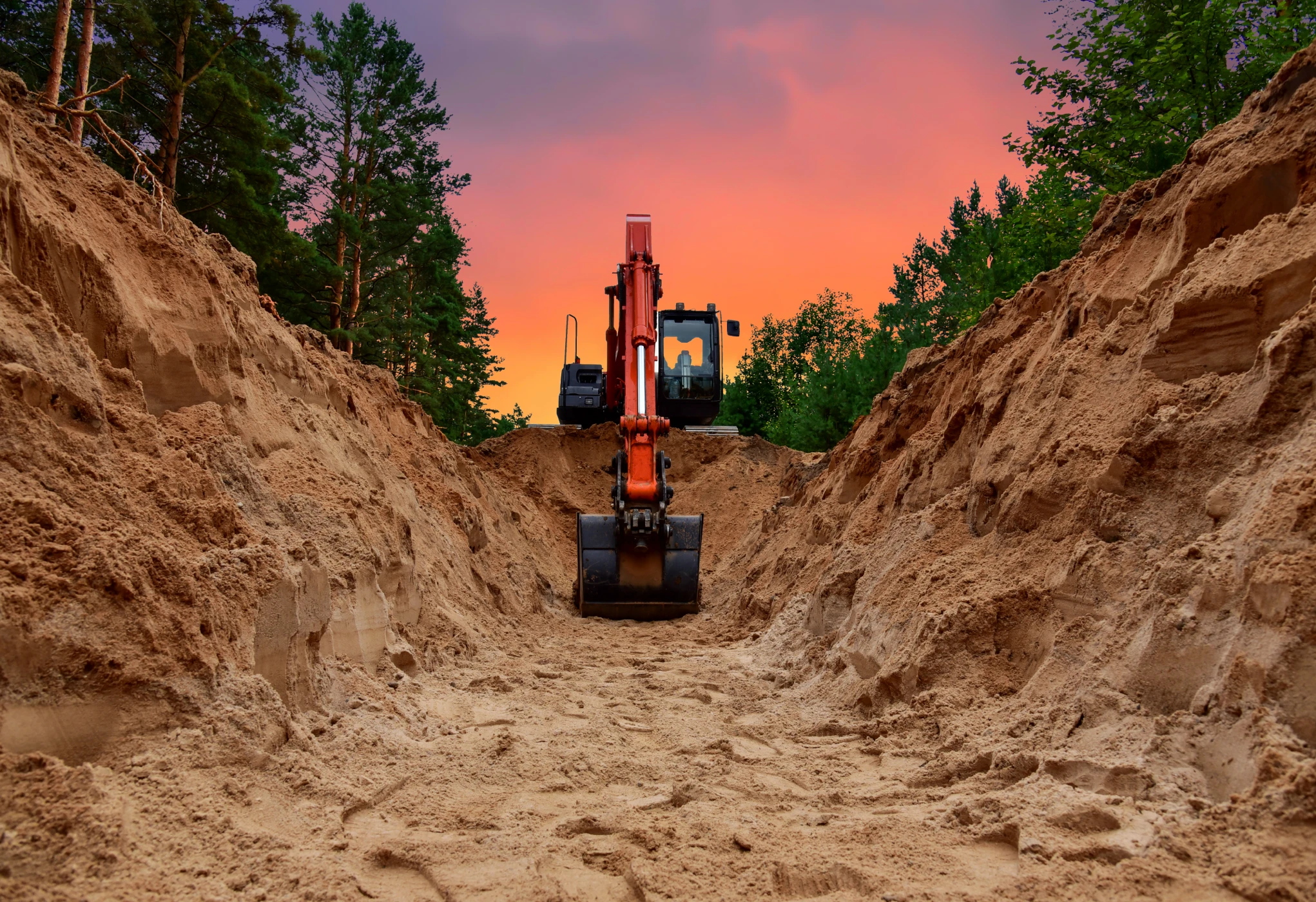 Excavator in deep trench at sunset